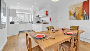 A modern kitchen with white cabinets, a wooden dining table set for four, and a large abstract painting on the wall.
