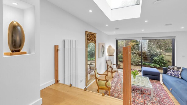 A modern living room with a skylight, a blue sofa, and a large mirror reflecting the garden outside.