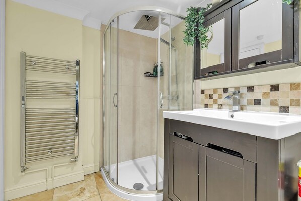 A modern bathroom with a glass shower enclosure, a white sink, and a tiled backsplash.