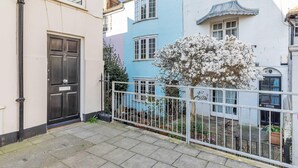 Une ruelle étroite avec une porte noire, une clôture en métal blanc et un bâtiment bleu aux ornements blancs.