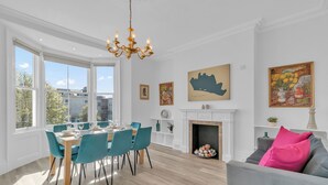 Un coin repas avec une table en bois et des chaises de couleur turquoise, un lustre et des œuvres d’art accrochées aux murs.