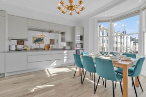 Una cucina moderna con mobili bianchi, un'area pranzo con sedie color acquamarina e un'ampia finestra con vista sulla città.