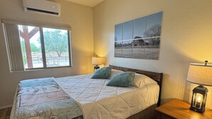 Un dormitorio con una cama grande, ventilador de techo, ventana con vistas, aire acondicionado de pared y una mesita de noche con lámpara.