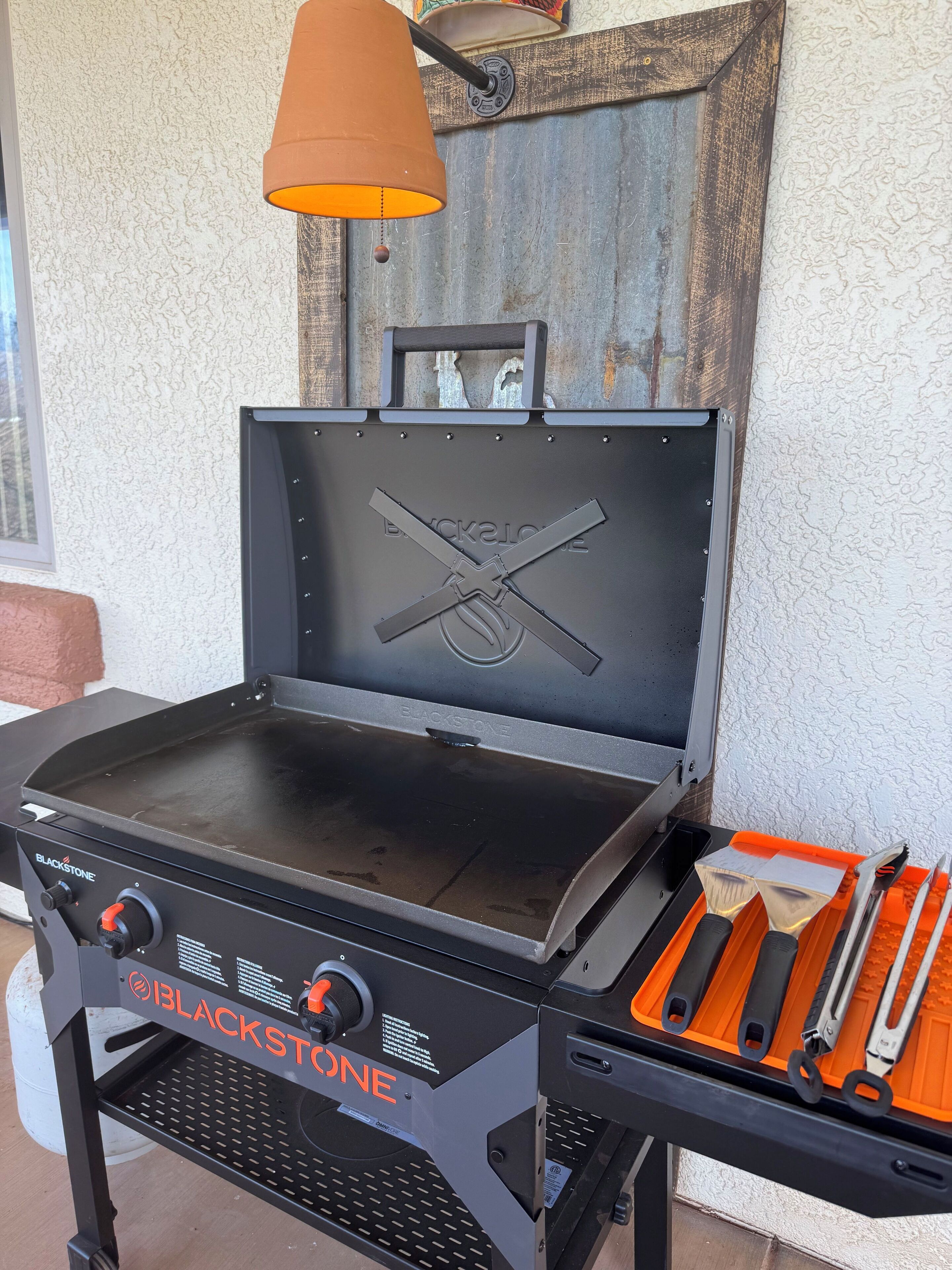 A Blackstone grill with a closed lid, a side table with grilling tools, and a hanging orange lamp.