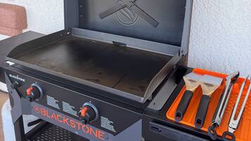 A Blackstone grill with a closed lid, a side table with grilling tools, and a hanging orange lamp.