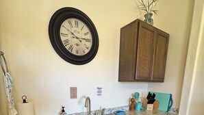Una cocina con un lavamanos doble, armarios de madera, un reloj en la pared y una planta en maceta encima de un armario.