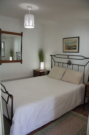 Un dormitorio con cama, mesita de noche, espejo, lámpara colgante y un cuadro en la pared.