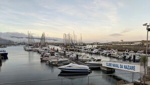 A marina with numerous boats docked, a sign reading "CLUBE NAVAL DA NAZARÉ", and a stone-paved walkway along the water. - Peaceful Farmhouse Retreat Near Nazaré | 3BR Countryside Stay Minutes to Beach (Quinta Nova, Famalicao, Portugal)