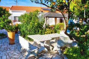 A patio with a table and chairs, surrounded by potted plants and a building with a tiled roof. - Peaceful Farmhouse Retreat Near Nazaré | 3BR Countryside Stay Minutes to Beach (Quinta Nova, Famalicao, Portugal)