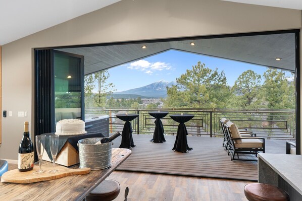 A spacious balcony with a wooden deck, three tables with black tablecloths, a bottle of wine, and a bucket of ice.
