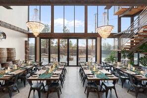 A dining area with multiple tables set for a meal, large windows, and a staircase.