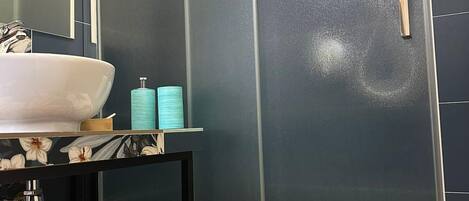 A bathroom with a white sink, a small table with toiletries, and a shower area with frosted glass doors.