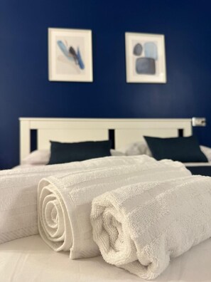 A neatly made bed with white linens and rolled white towels, a white headboard, and two framed pictures on the wall. - Binario 73 (Naples)