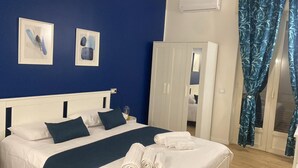 A neatly made bed with white linens and dark blue bedding, a white wardrobe, and two framed artworks on the wall. - Binario 73 (Naples)