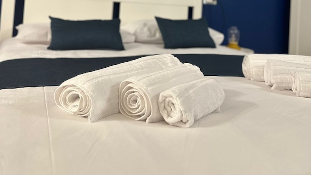 A neatly made bed with white linens and rolled towels, a white headboard, and two framed pictures on the wall. - Binario 73 (Naples)
