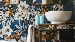 A bathroom with a floral wallpaper, a white sink, a bidet, and a trash can. - Binario 73 (Naples)