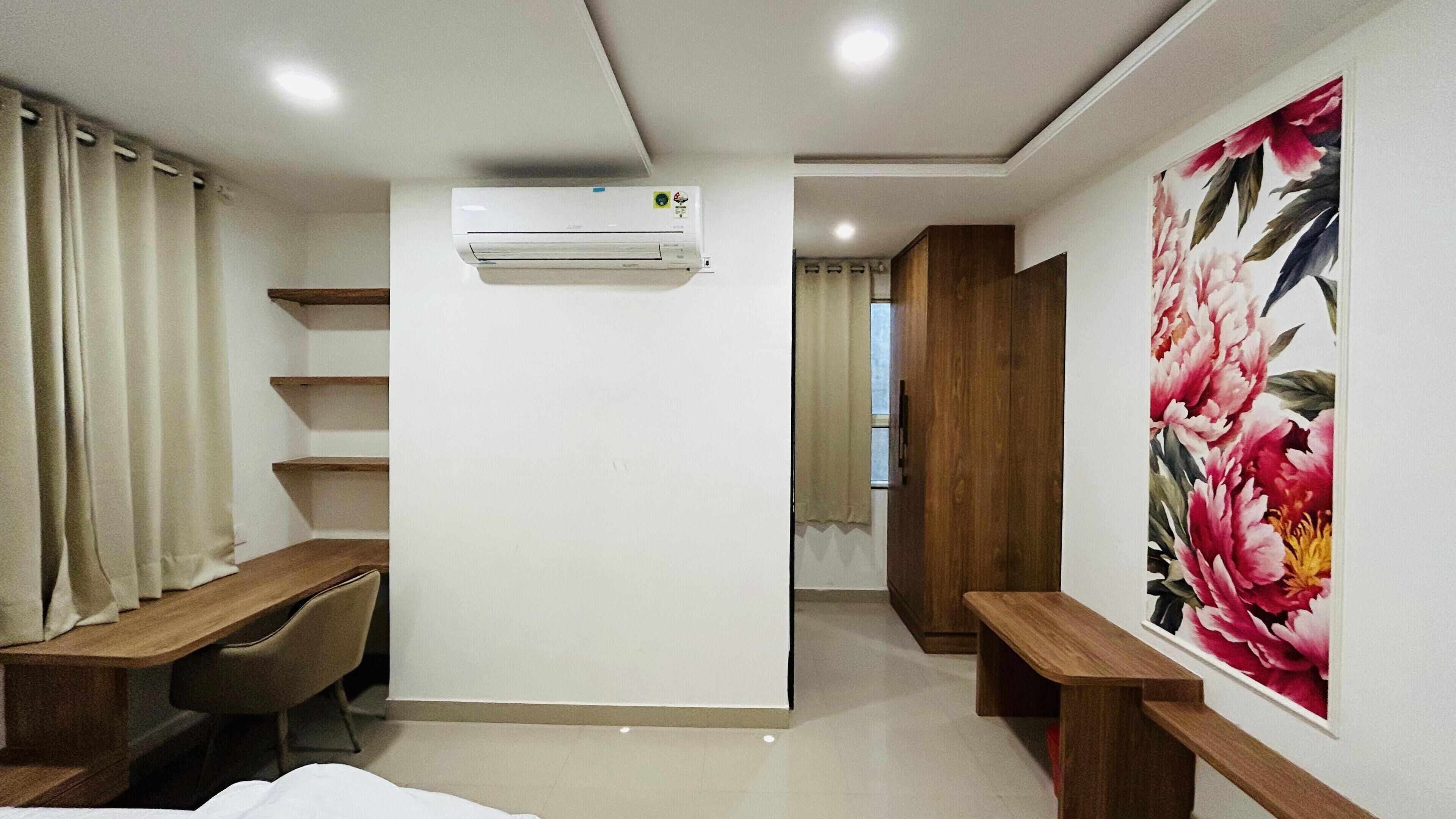 A bedroom with a bed, a desk, a chair, a wardrobe, an air conditioning unit, and a large floral painting on the wall.