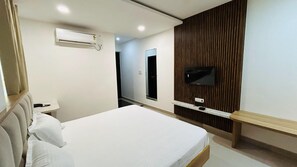A hotel room with a bed, bedside table, air conditioning unit, and a mounted TV. - The Gamora Hotel (Gwalior)