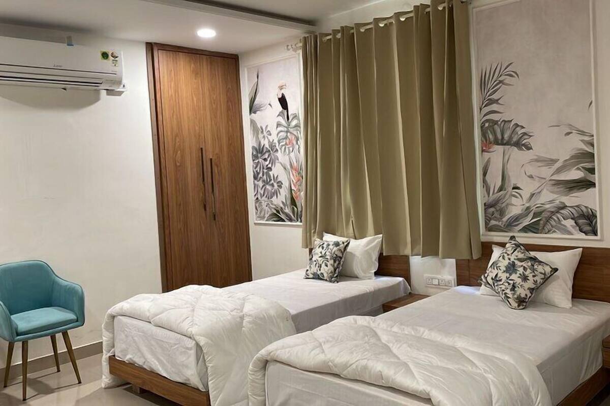 A hotel room with two single beds, a wooden wardrobe, a blue chair, and floral wall art.