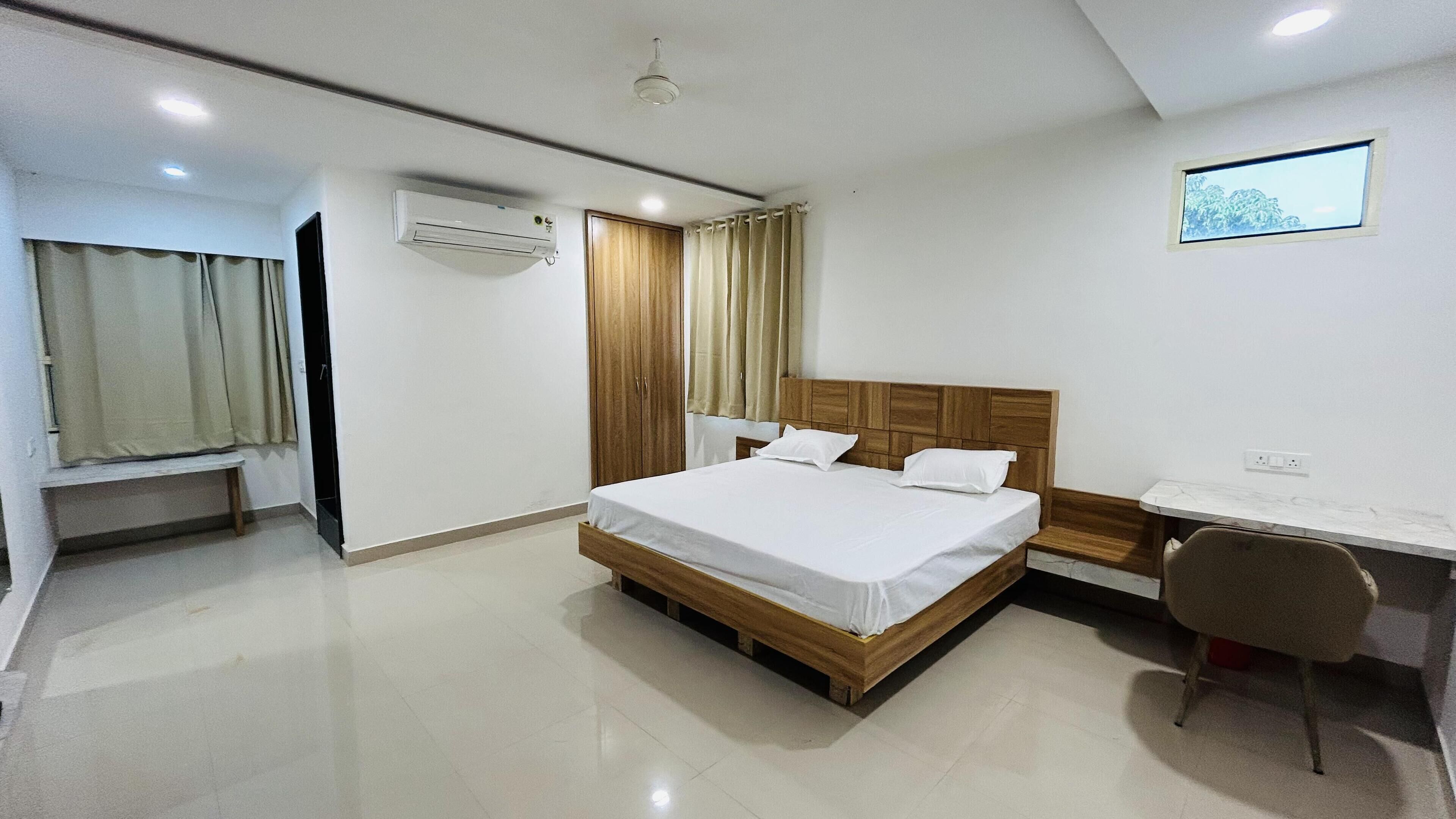 A hotel room with a bed, a desk, a chair, an air conditioning unit, and a window with curtains.
