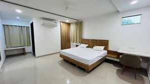 A hotel room with a bed, a desk, a chair, an air conditioning unit, and a window with curtains. - The Gamora Hotel (Gwalior)