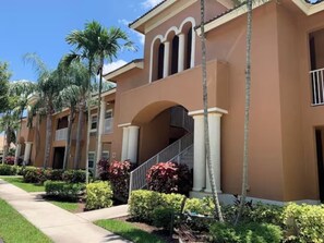 A multi-story building with a central staircase, palm trees, and well-maintained landscaping.