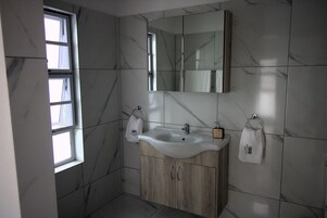 Un baño con pared de azulejos de mármol, tocador de madera, lavamanos y espejo.