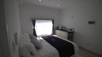 Un dormitorio con cama, escritorio, microondas y hervidor.