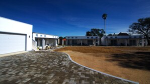 A modern building with a white facade, a covered driveway, and a clear blue sky. - Little Bush Guesthouse (Omaruru)