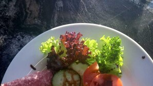 A plate with scrambled eggs, bacon, a slice of tomato, a cucumber, a slice of salami, and mixed greens. - Little Bush Guesthouse (Omaruru)