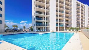 Une piscine située à côté d’un hôtel à plusieurs étages, doté de balcons et d’un espace de détente extérieur.