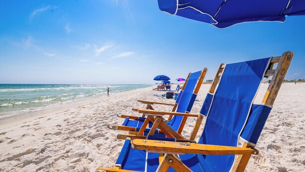 Une plage bordée de rangées de chaises longues et de parasols en bois.