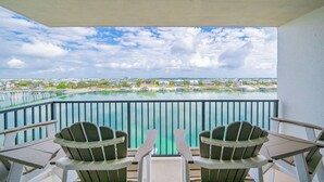 Un balcon avec deux fauteuils Adirondack, une vue sur le bord de l’eau, avec des bâtiments et un pont.