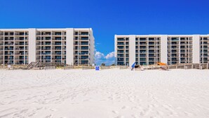 Un hôtel en bord de mer, avec plusieurs étages, des balcons et une plage de sable au premier plan.