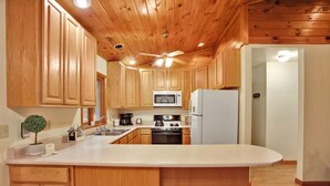 A kitchen with wooden cabinets, a microwave, a stove, and a refrigerator. - Wellsboro Woods Retreat - Near 2 State Parks (Middlebury Township)