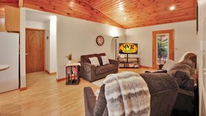 A cozy living room with wooden ceilings, a brown sofa, a coffee table, and a sign for MVR Vacation Rentals. - Wellsboro Woods Retreat - Near 2 State Parks (Middlebury Township)
