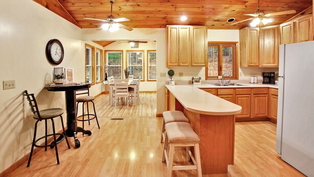 A kitchen with wooden cabinets, a dining area with a table and chairs, and a bar area with stools. - Wellsboro Woods Retreat - Near 2 State Parks (Middlebury Township)