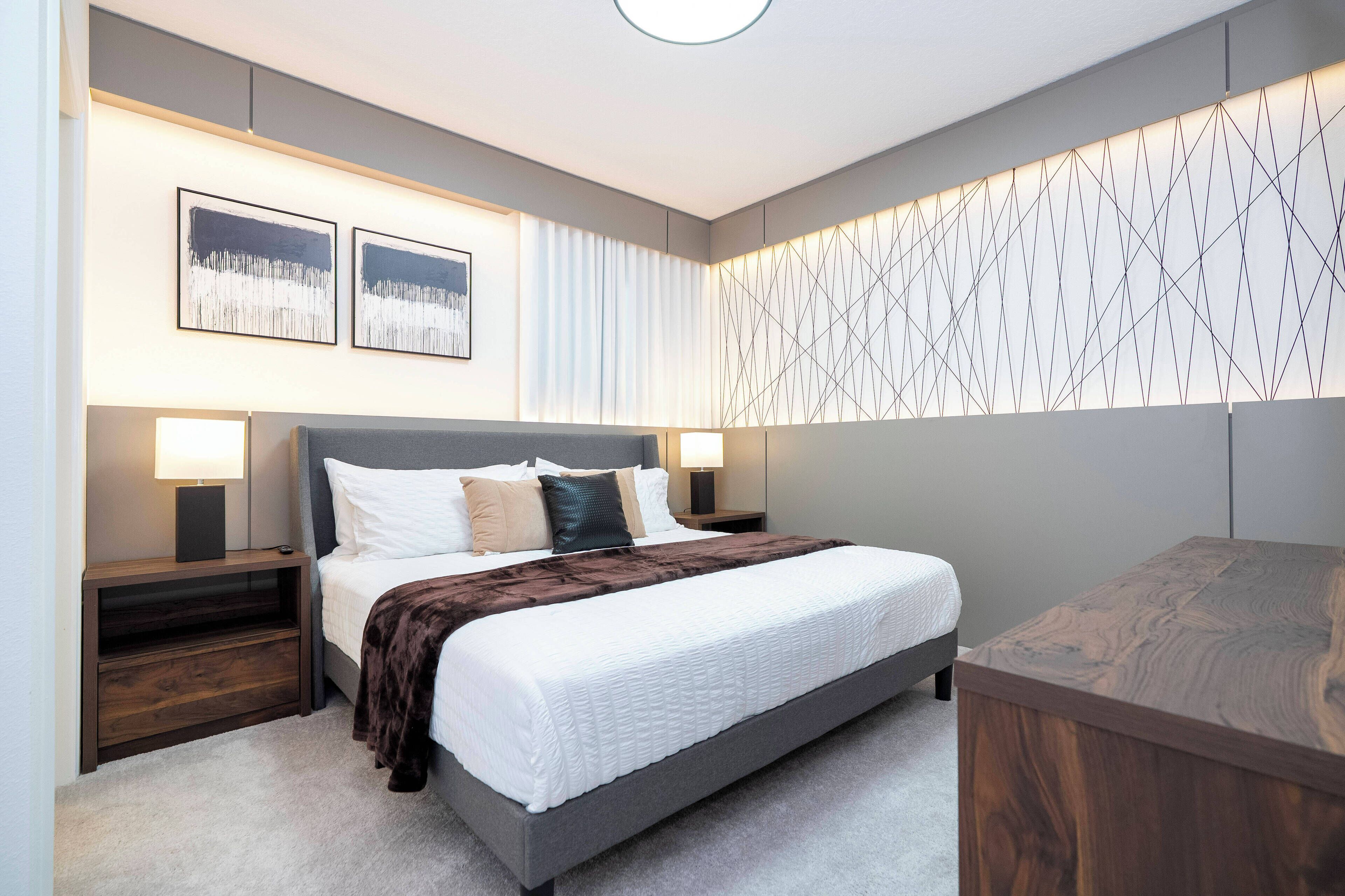 Une chambre moderne avec un grand lit, deux tables de chevet avec des lampes, une tête de lit et un mur orné d’un motif géométrique.