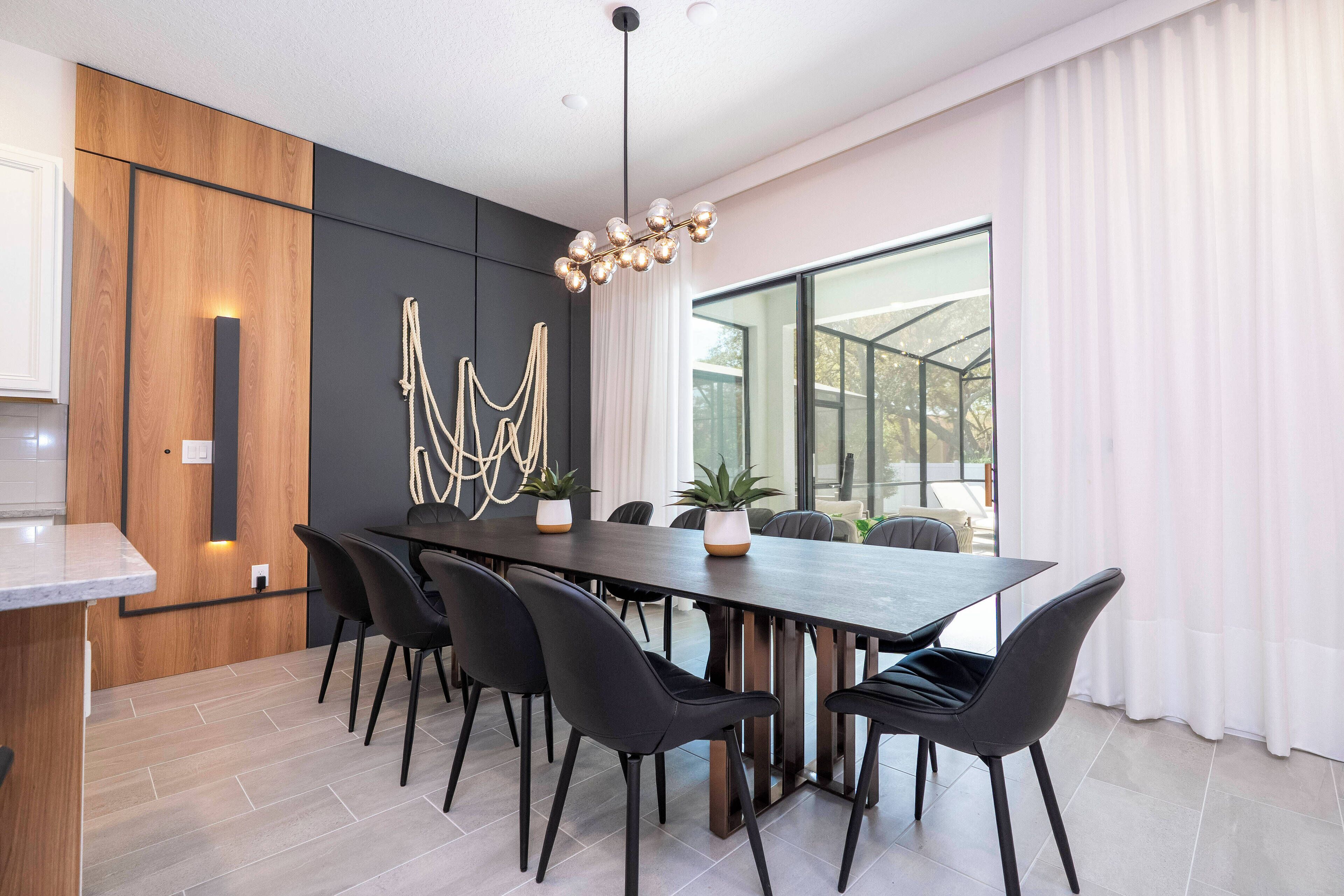 A modern dining area with a long table, black chairs, and a unique chandelier.