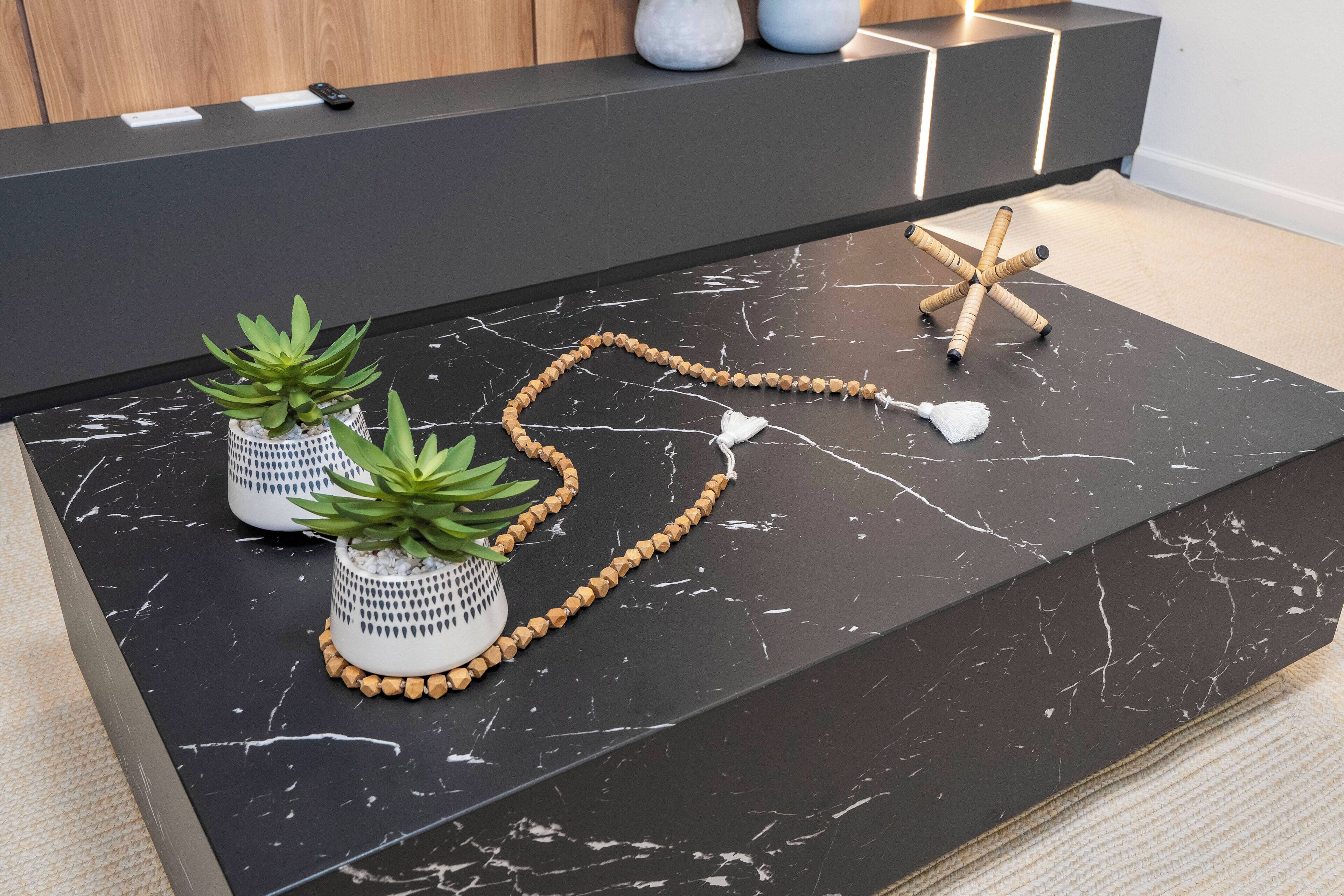 A black marble countertop with two potted succulents, a beaded necklace, and a starfish.