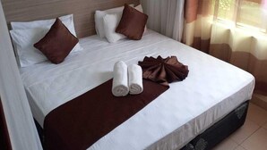 A neatly made bed with white linens, brown pillows, and a brown throw blanket. - Blodriff Apartments (Mombasa)