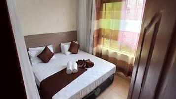 Una cama bien hecha con almohadas y una colcha, un ventilador de techo y una ventana con cortinas.