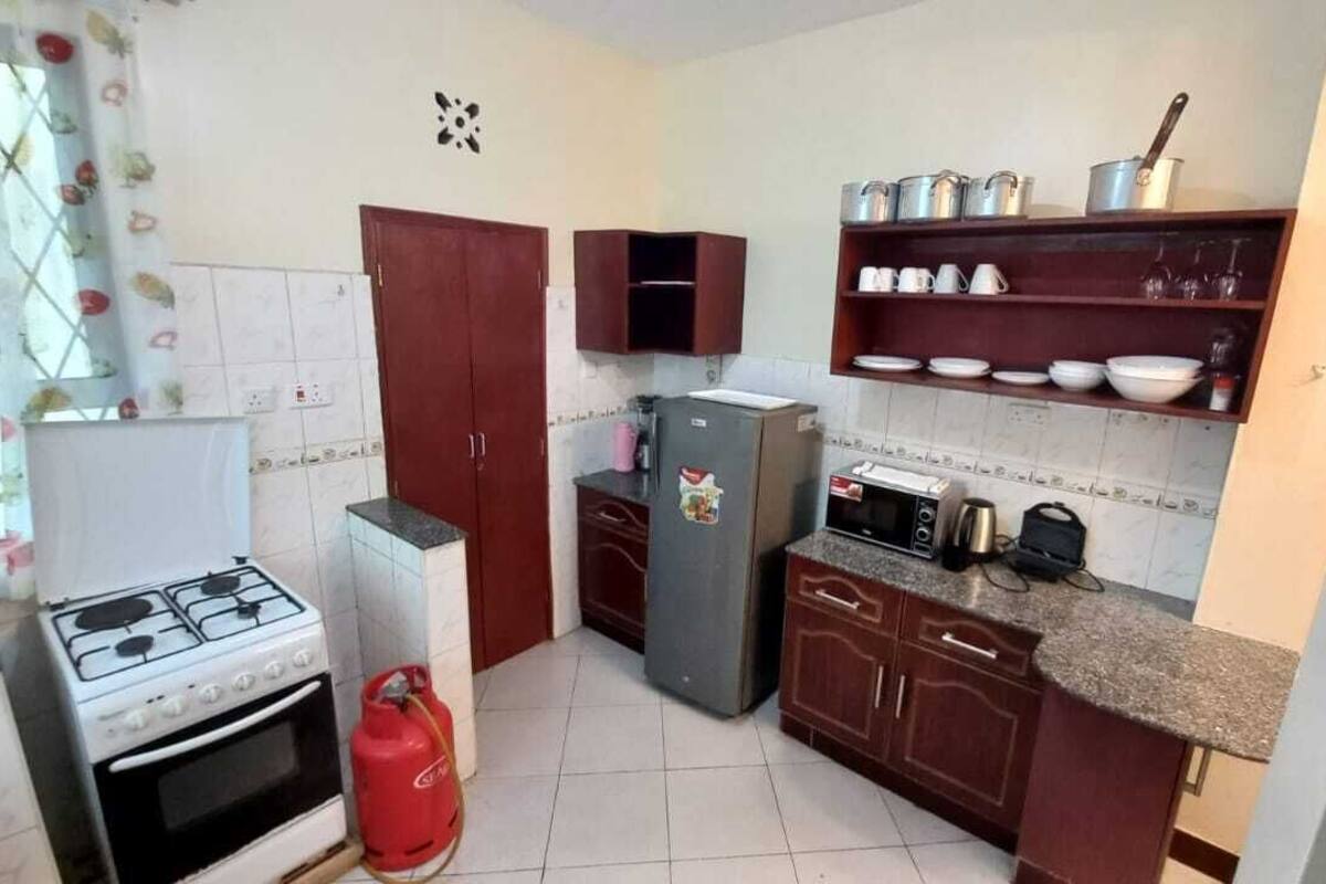 A compact kitchen with a gas stove, a refrigerator, a microwave, and a gas cylinder.