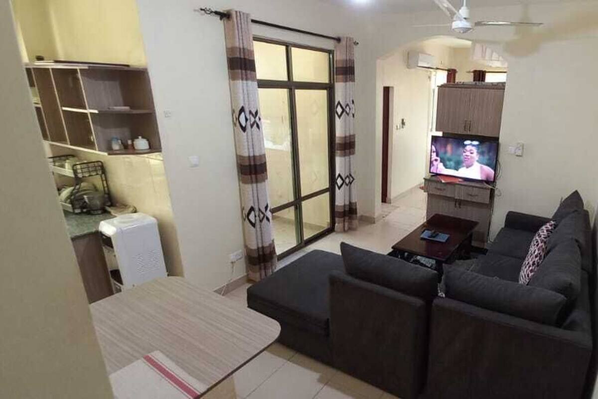 A living room with a sofa, a coffee table, a television, and a sliding glass door leading to a balcony.