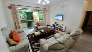 A living room with a sofa set, a coffee table, and a TV mounted on the wall. - Blodriff Apartments (Mombasa)