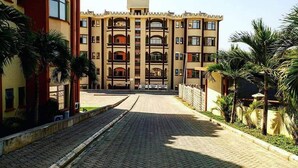 A multi-story building with a central courtyard, surrounded by palm trees and a paved walkway. - Blodriff Apartments (Mombasa)