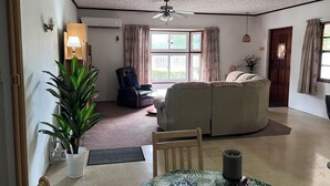 A living room with a sofa, a chair, a dining table with a candle, and a ceiling fan.