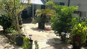A courtyard with potted plants, a tiled floor, and a building with a sloped roof.