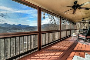 A covered outdoor deck with a wooden railing, a ceiling fan, string lights, and a view of mountains. - Dee's Cozy Cottage (Waynesville)