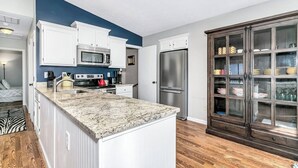 Une cuisine moderne avec des meubles blancs, un plan de travail en granit, un réfrigérateur en acier inoxydable et un meuble en bois doté de portes en verre.